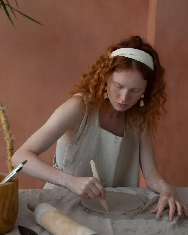 Woman shaping a clay plate at a studio worktable