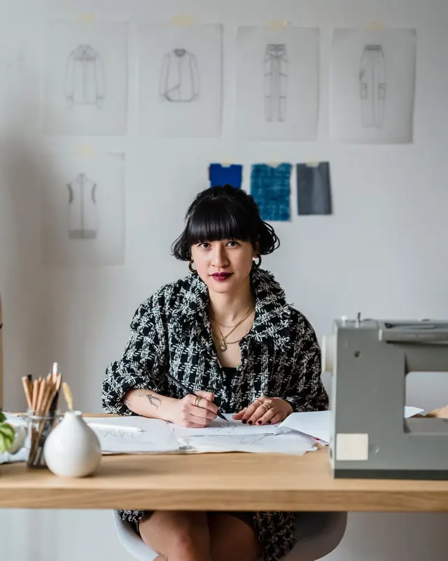 Designer sketching at a desk in front of pinned clothing drawings