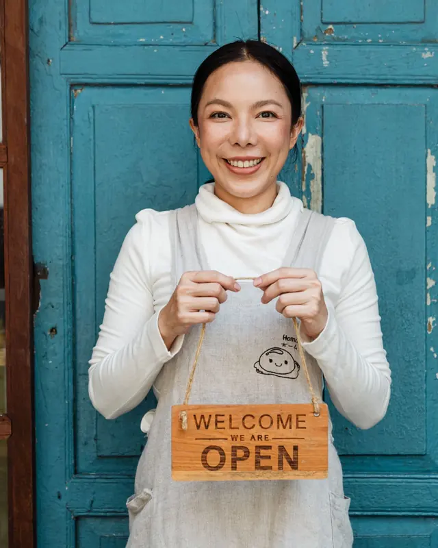 Smiling café owner holding a “Welcome, we are open” sign