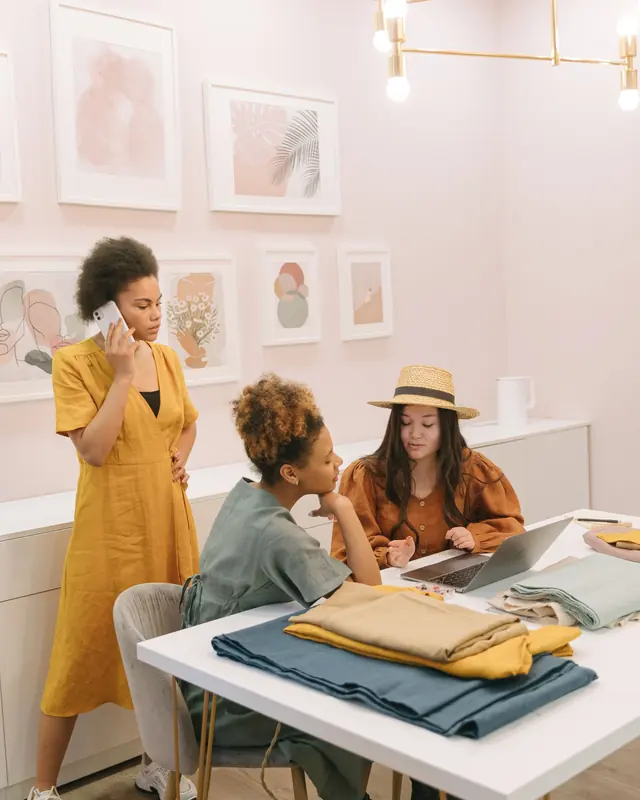 Three women working together around a laptop in a bright studio